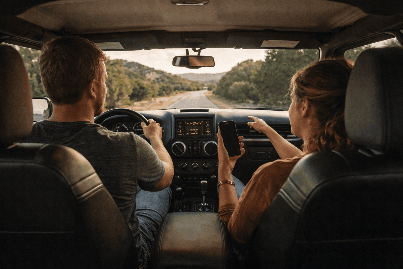 hill-country-couple-jeep-interior-road-trip-navigation A couple in a Jeep seen from the back seat, the passenger gesturing toward the road ahead during a Hill Country drive.